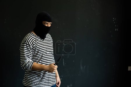 Foto de El cuchillo enmascarado en su mano. El ladrón amenaza con una daga. Bandido en máscara negra con cuchillo - Imagen libre de derechos