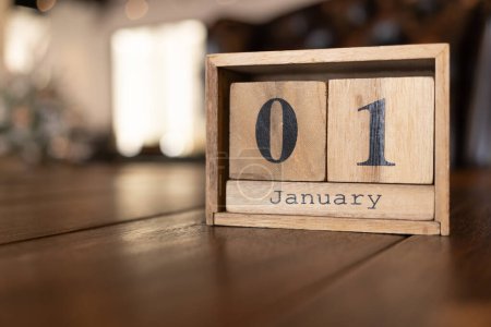 Würfelförmiger Kalender für den 01. Januar auf Holzoberfläche. Ziegelkalender aus Holz mit eingraviertem Datum 01. Januar steht auf einem Schreibtisch. 