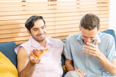 Photo for Two men in casual outfits sitting on sofa embracing and watching TV with beer and pizza in living room at home. LGBT gay relationship concept. - Royalty Free Image