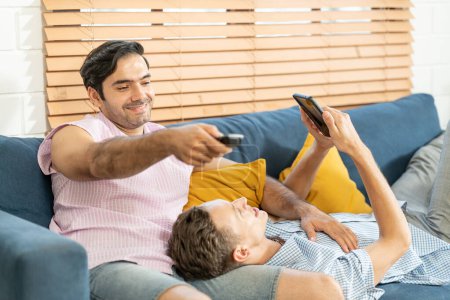 Foto de Dos hombres en trajes casuales sentados en el sofá abrazando y viendo la televisión con cerveza y pizza en la sala de estar en casa. Concepto de relación gay LGBT. - Imagen libre de derechos