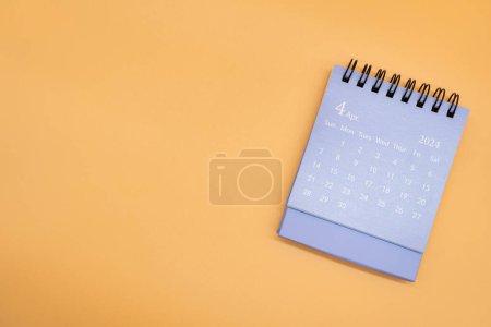 Blauer Tischkalender für April 2024 isoliert auf orangefarbenem Hintergrund. Kalenderkonzept mit Kopierraum. Flache Lage.