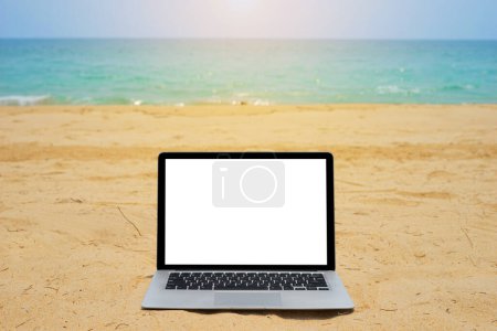 Photo for Laptop with blank screen for creative design on sand beach nearby blue sea background with sun ray effect. Computer notebook with monitor clipping path for present landing page design mock up template - Royalty Free Image