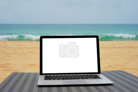 Photo for Laptop with blank screen for creative design on beach bed nearby beach and blue sea background. Computer notebook with clipping path for present landing page design mock up template - Royalty Free Image