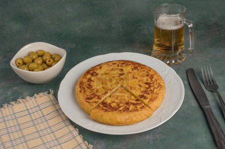plate with Spanish potato omelet next to a bowl of olives and a mug of beer