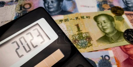 Photo for Next fiscal year 2023 on the calculator screen against the background of Chinese banknotes and coins. The influence of the Chinese currency on the world economy. Coins 1 yuan and 5 jiao in the background. Energy crisis and economic slowdown - Royalty Free Image