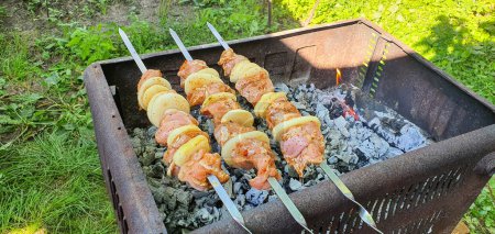 Photo for Pieces of pork with onions on skewers are grilled close-up. Traditional kebabs that are prepared for the holidays in Ukraine. The meat has just begun to fry and it is in the initial stage of frying - Royalty Free Image
