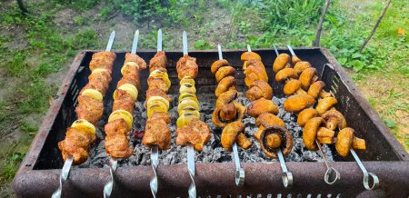 Photo for Pieces of pork with onions and champignon mushrooms on skewers are grilled close-up. Traditional kebabs that are prepared for the holidays in Ukraine. The meat is well cooked and ready to eat - Royalty Free Image
