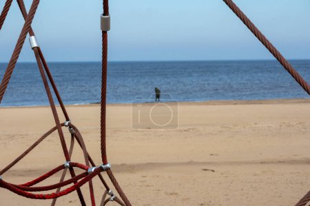 Photo for Red rope sections fastened with a metal clamp on a background of brown sand and blue sea - Royalty Free Image