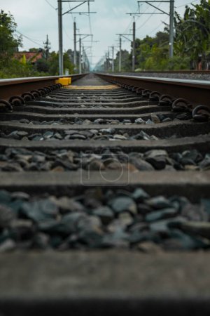Téléchargez les photos : Détail des voies ferrées en fer, bois et gravier dans une banlieue par une journée nuageuse et sombre en Indonésie - en image libre de droit