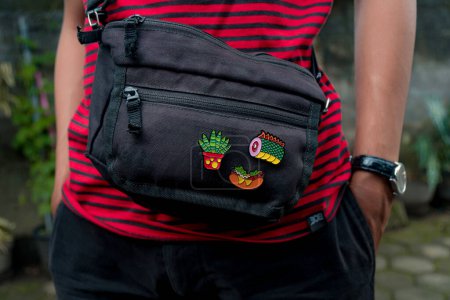 Téléchargez les photos : Séance photo de produit de broche acrylique sur un sac noir uni qu'un homme porte, détail d'une broche en émail faite main produit attaché à un sac à bandoulière - en image libre de droit