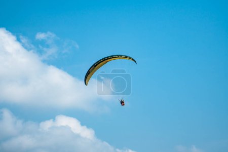 Photo for An adrenaline-pumping extreme sport, paragliding against the clear blue sky. Paraglider flying with his parachute above the sky with a background of blue sky and white clouds in a sunny day. - Royalty Free Image