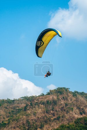 Photo for Paragliding attraction flying across hilly areas and clear blue skies. Paragliding is a sport that stimulates adrenaline by flying using a parachute in the wide sky - Royalty Free Image