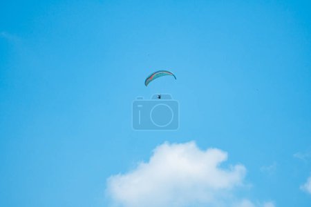 Photo for An adrenaline-pumping extreme sport, paragliding against the clear blue sky. Paraglider flying with his parachute above the sky with a background of blue sky and white clouds in a sunny day. - Royalty Free Image