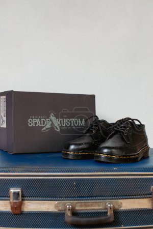 Téléchargez les photos : Chaussures de brogue à bout d'aile noires classiques en cuir véritable exposées sur une boîte à chaussures noire et une valise vintage portée. Concept photo de chaussures vintage avec un style classique - en image libre de droit