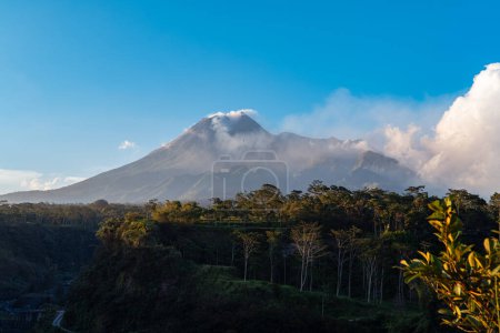 The beauty of Mount Merapi at dusk before dark with a cliff of cold lava flows right in front of it. Mount Merapi looks detailed on a clear day with blue sky and clouds beside it