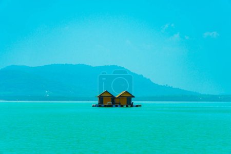 Small floating houses between the horizon line that separates the sea from the sky and set against a backdrop of plains and mountains. Floating houses used by fishermen as a place to cultivate fish