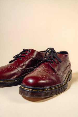 A man's hand holds a maroon brogue wingtip shoes with a rubber outsole made from genuine cowhide. Men's hands holding elegant and shiny vintage shoes on a cream background