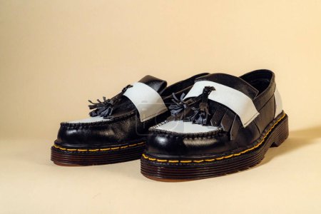 Cierre de zapatos de borla en blanco y negro con suela de goma hecha de cuero de vaca genuino. Estudio de un elegante y brillante producto de zapatos vintage de dos tonos sobre un fondo beige