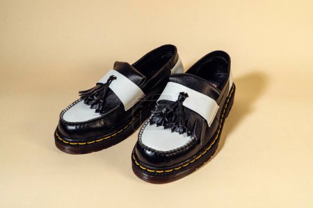 Close up of black and white tassel shoes with rubber outsole made from genuine cow leather. Studio shot of an elegant and shiny two tone vintage shoe product on a beige background