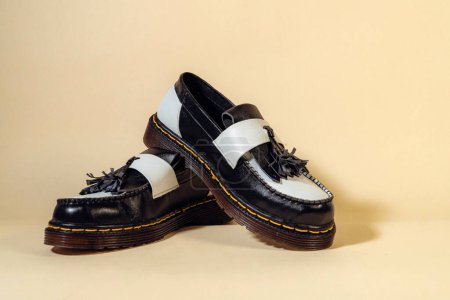 Nahaufnahme von schwarz-weißen Quasten-Schuhen mit Gummi-Außensohle aus echtem Rindleder. Studioaufnahme eines eleganten und glänzenden zweifarbigen Vintage-Schuhs auf beigem Hintergrund
