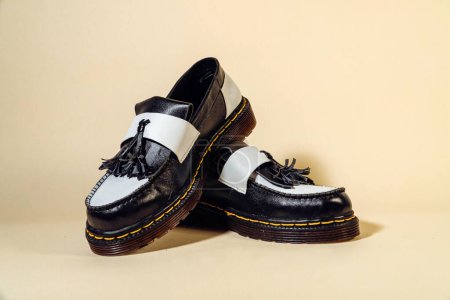 Nahaufnahme von schwarz-weißen Quasten-Schuhen mit Gummi-Außensohle aus echtem Rindleder. Studioaufnahme eines eleganten und glänzenden zweifarbigen Vintage-Schuhs auf beigem Hintergrund