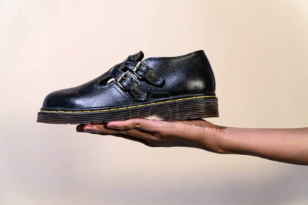 A man's hand holds a black Mary Jane Rockabilly shoe with a rubber outsole made from genuine cowhide. Men's hands holding elegant and shiny vintage shoes on a cream background