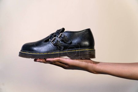 A man's hand holds a black Mary Jane Rockabilly shoe with a rubber outsole made from genuine cowhide. Men's hands holding elegant and shiny vintage shoes on a cream background