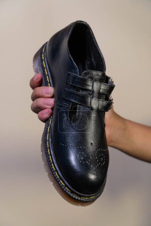La main d'un homme tient une chaussure Mary Jane Rockabilly noire avec une semelle extérieure en caoutchouc faite de cuir de vache véritable. Les mains des hommes tenant des chaussures vintage élégantes et brillantes sur un fond crème