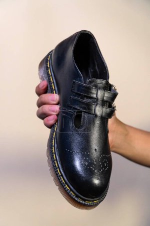 La mano de un hombre sostiene un zapato Mary Jane Rockabilly negro con una suela de goma hecha de piel de vaca genuina. Manos de los hombres sosteniendo zapatos vintage elegantes y brillantes sobre un fondo crema