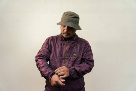 Half body portrait of mature Asian man with beard and mustache posing in ready style before traveling. Mature man wearing adventure outfit with jacket and bucket hat isolated on beige background.