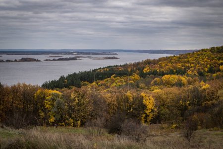 Panoramic view of yellow trees, a wooden hut and the river on an autumn cloudy day.