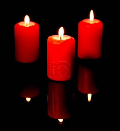 Photo for Three burning red candles are reflected in a black mirror background. - Royalty Free Image