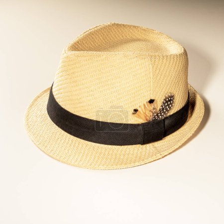 Foto de Sombrero de sol con una cinta y una pluma de pájaro hecha de paja ligera para las vacaciones sobre un fondo claro. - Imagen libre de derechos
