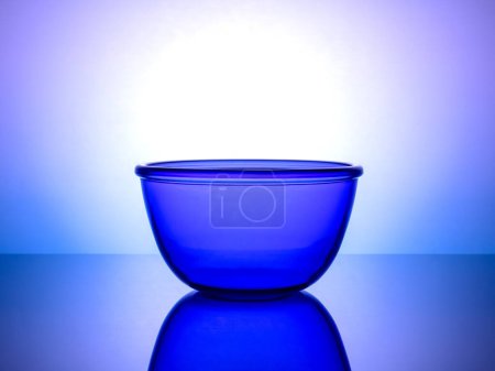 Stylish blue glass dinnerware set on a glowing gradient background, perfect for chic culinary presentation. The elegant tableware stands out and adds a touch of sophistication to any dining setting.