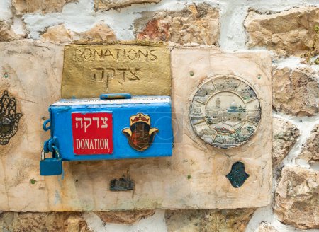 Photo for Safed, Israel, July 01, 2023 : A donation box and a coat of arms with the symbols of Jerusalem are pinned to a stone wall in the Safed city old part of in northern Israel - Royalty Free Image