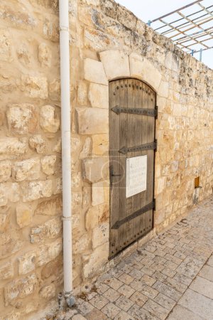 Photo for Safed, Israel, July 01, 2023 : Antique wooden door with forged hinges in a stone wall on a quiet street in the old part of Safed city in northern Israel - Royalty Free Image