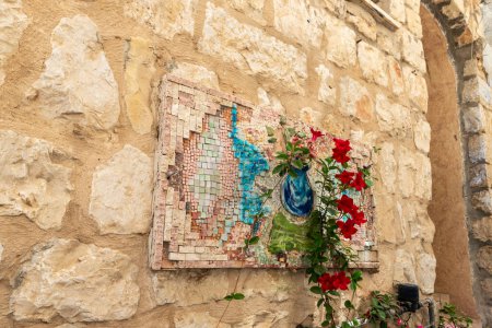 Photo for A large decorative mosaic on the stone wall of a residential building and flowers standing nearby on a quiet street in the old part of Safed city in northern Israel - Royalty Free Image