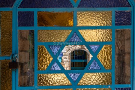 Photo for Safed, Israel, July 01, 2023 : A look through the entrance gate decorated with stained-glass windows at the door of the synagogue on a quiet street in the old part of Safed city in northern Israel - Royalty Free Image