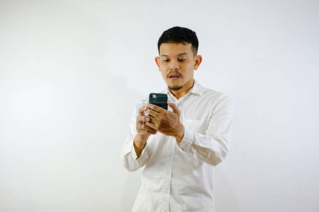 Photo for Adult Asian man showing confused expression when looking to his phone - Royalty Free Image