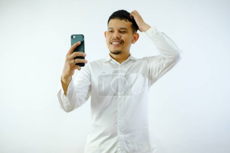 Photo for Adult Asian man showing confused expression when looking to his phone - Royalty Free Image