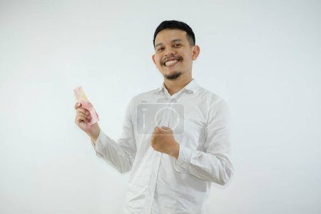Téléchargez les photos : Adulte asiatique l'homme serré poing tout en tenant papier-monnaie et montrant heureux expression - en image libre de droit