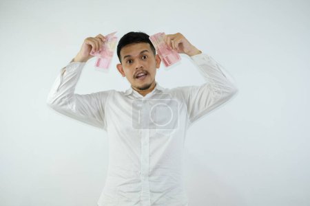 Foto de Adulto asiático hombre sosteniendo papel moneda y mostrando confusa cara expresión - Imagen libre de derechos