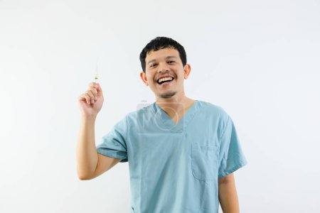 Téléchargez les photos : Jeune asiatique homme médecin sourit tout en tenant la seringue sur sa main, montrant une expression heureuse. Isolé sur fond blanc. Concept médical et de santé. - en image libre de droit