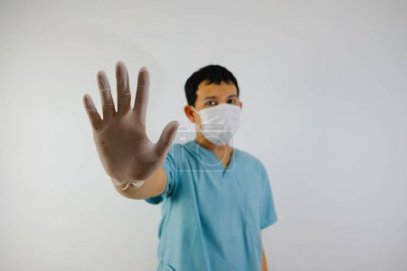 Téléchargez les photos : Un jeune homme asiatique vêtu d'une combinaison de gommage et d'un masque facial montrant un geste d'arrêt de la main, gros plan de la main. - en image libre de droit
