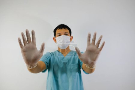 Téléchargez les photos : Un jeune homme asiatique vêtu d'une combinaison de gommage et d'un masque facial montrant un geste d'arrêt de la main, gros plan de la main. - en image libre de droit