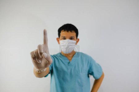 Photo for A young asian man wearing scrub suit and face mask showing stop hand gesture, close up of the hand. - Royalty Free Image