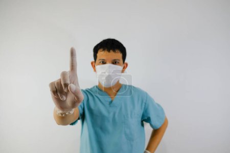 Photo for A young asian man wearing scrub suit and face mask showing stop hand gesture, close up of the hand. - Royalty Free Image