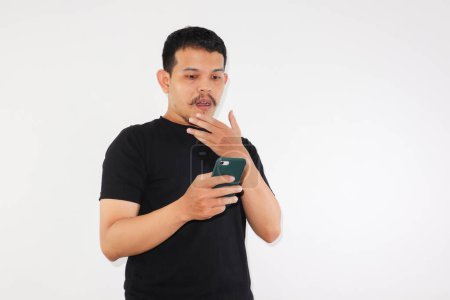 Photo for Adult Asian man showing confused and shocked expression when looking to his phone - Royalty Free Image