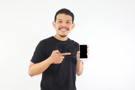 Foto de Adulto asiático hombre sonriendo feliz mientras muestra la pantalla del teléfono móvil en blanco y apuntando a ella - Imagen libre de derechos