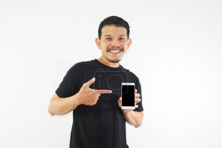 Téléchargez les photos : Adulte asiatique homme souriant heureux tout en montrant écran de téléphone portable vierge et pointant sur elle - en image libre de droit